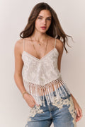 Woman wearing a white lace top with fringe and blue jeans on a plain background