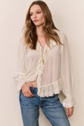 Woman wearing a white blouse with ruffled lace details and blue jeans against a plain background