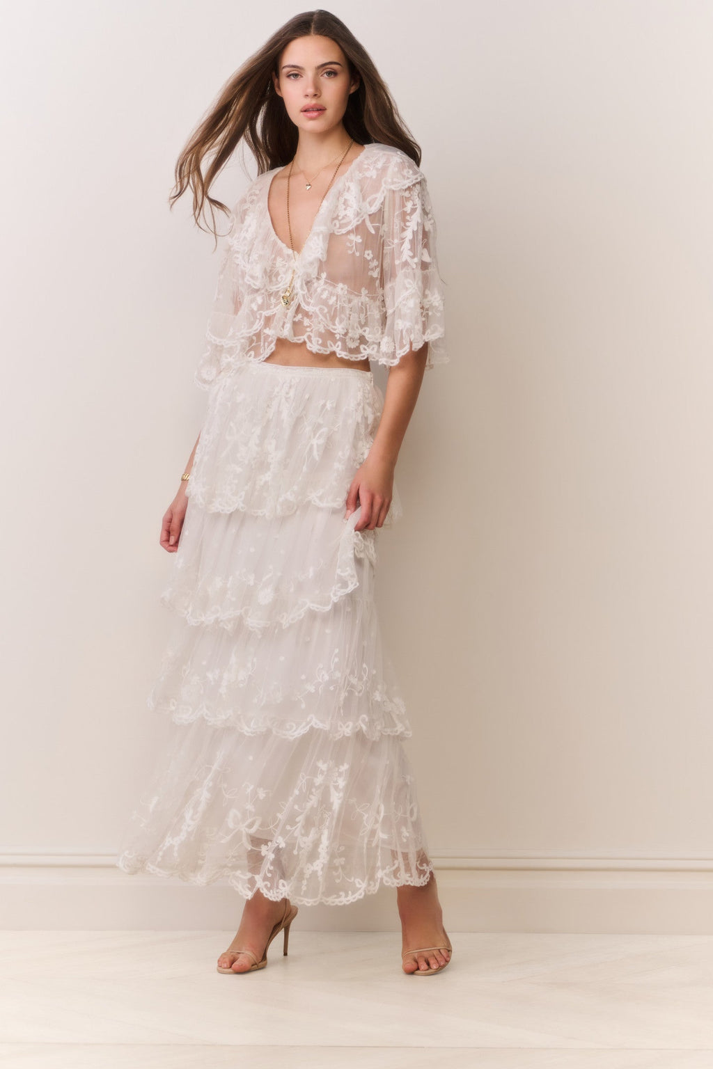 Woman wearing a white lace top and matching tiered skirt against a plain background