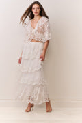 Woman wearing a white lace top and matching tiered skirt against a plain background