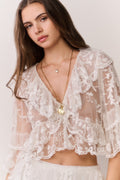 Woman wearing a sheer lace top and matching tiered skirt with a plain background