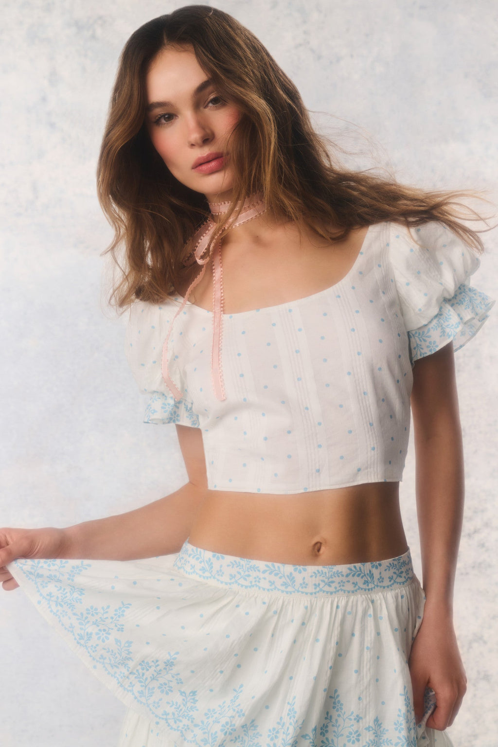 Woman wearing a light-colored outfit with floral patterns against a plain background
