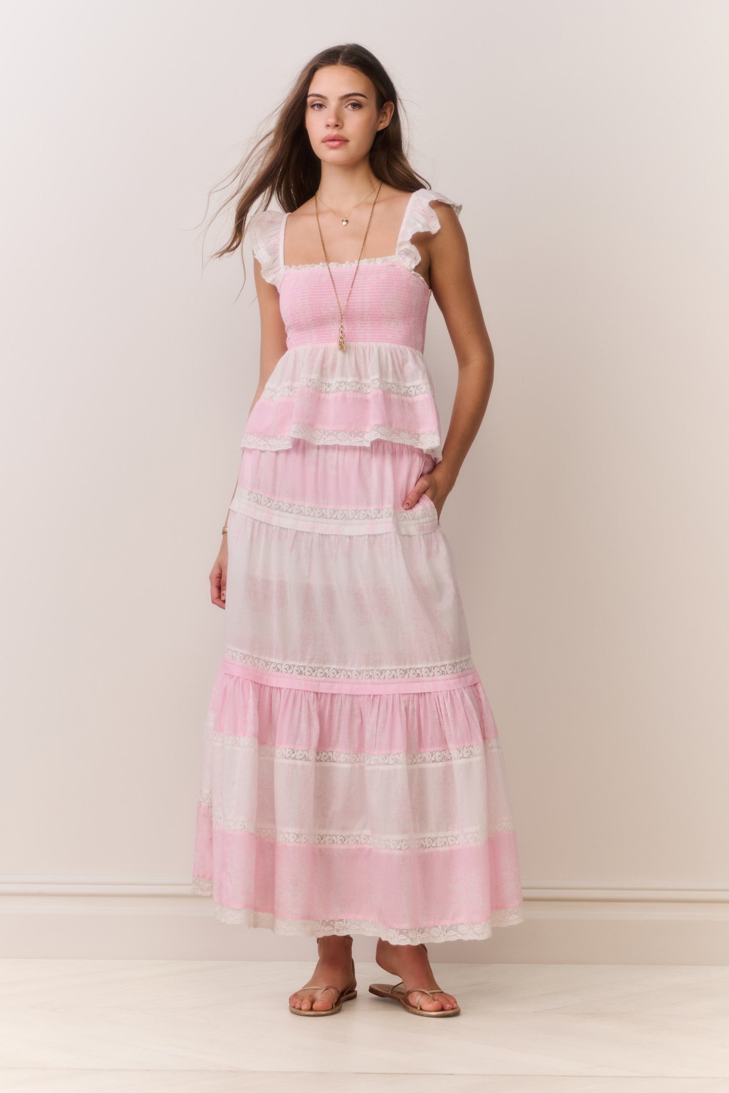 Woman wearing a pink and white ruffle top and matching skirt with a plain background