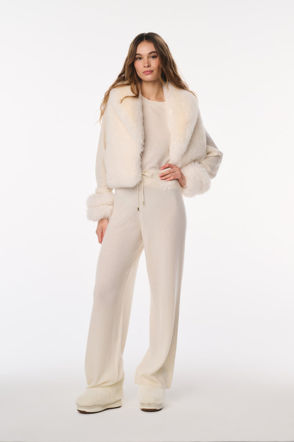 Woman wearing a cream-colored outfit with fur trim on a white background