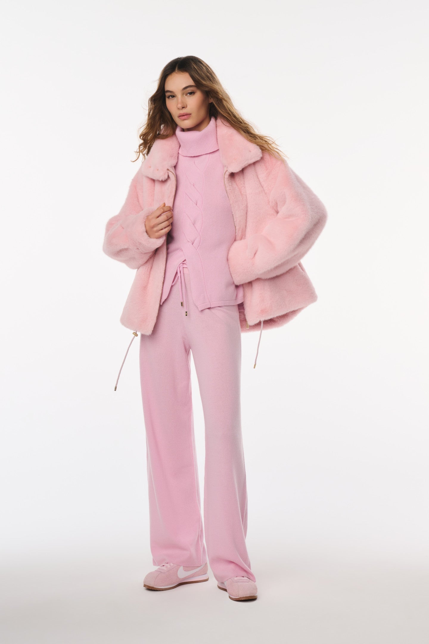 Woman wearing a pink outfit with a matching coat on a white background