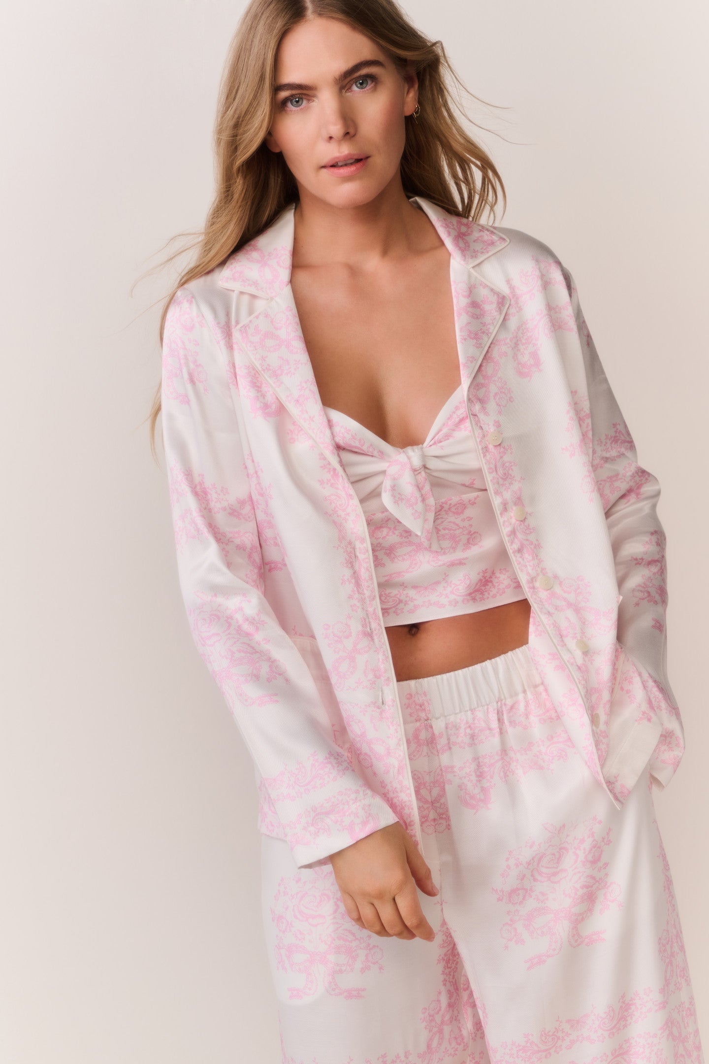 Person wearing a pink and patterned button down and matching pants outfit on a plain background